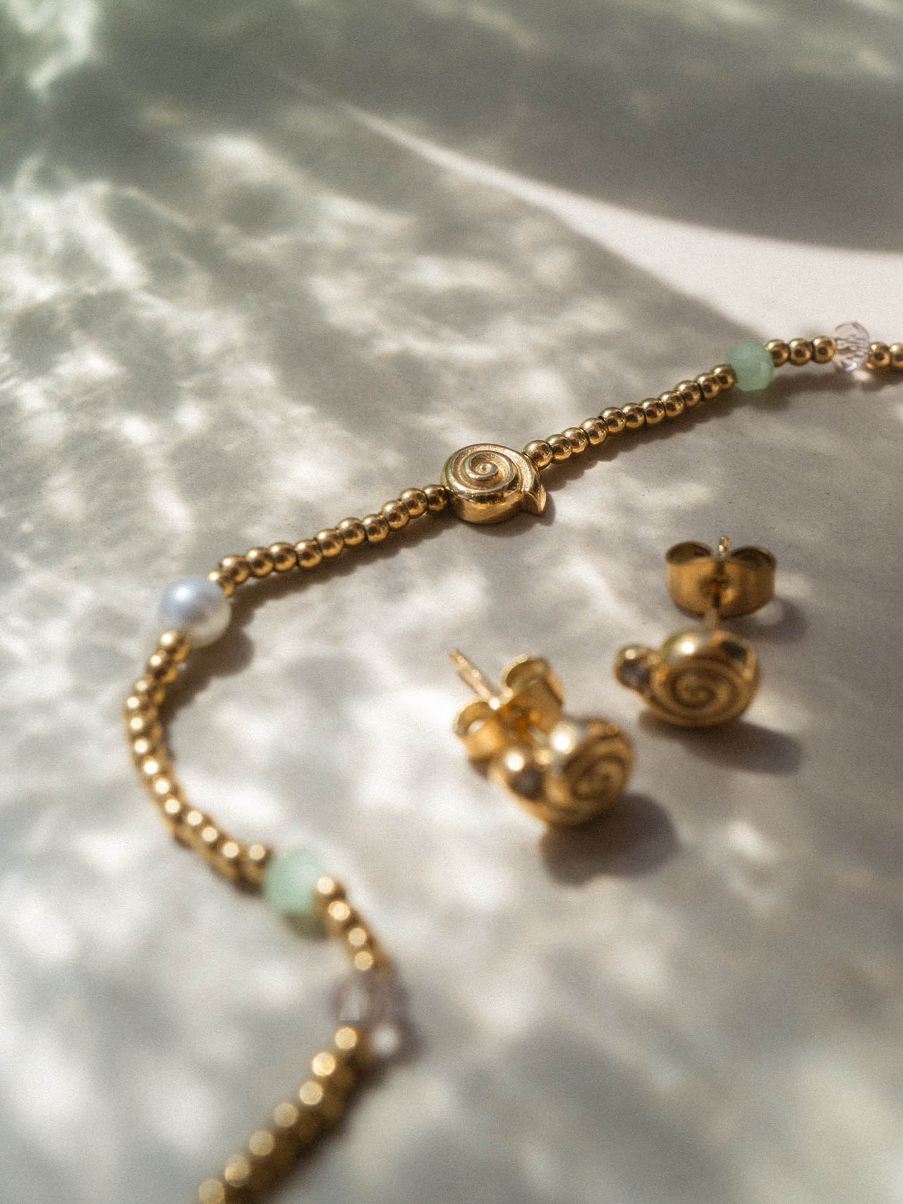 Silberne PURELEI Ohrringe und Armband mit spiralförmigem Design auf sanftem Hintergrund.