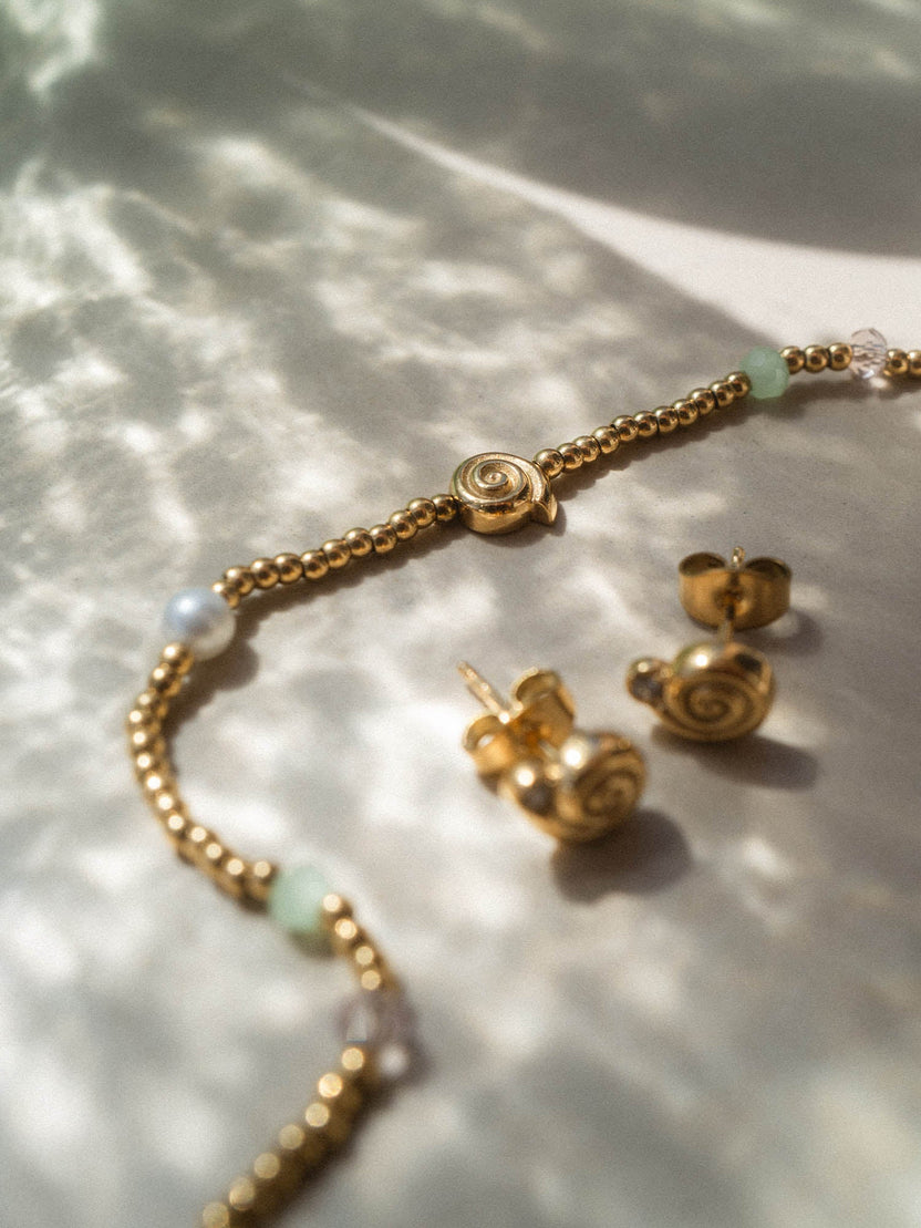 Silberne PURELEI Ohrringe und Armband mit spiralförmigem Design auf sanftem Hintergrund.