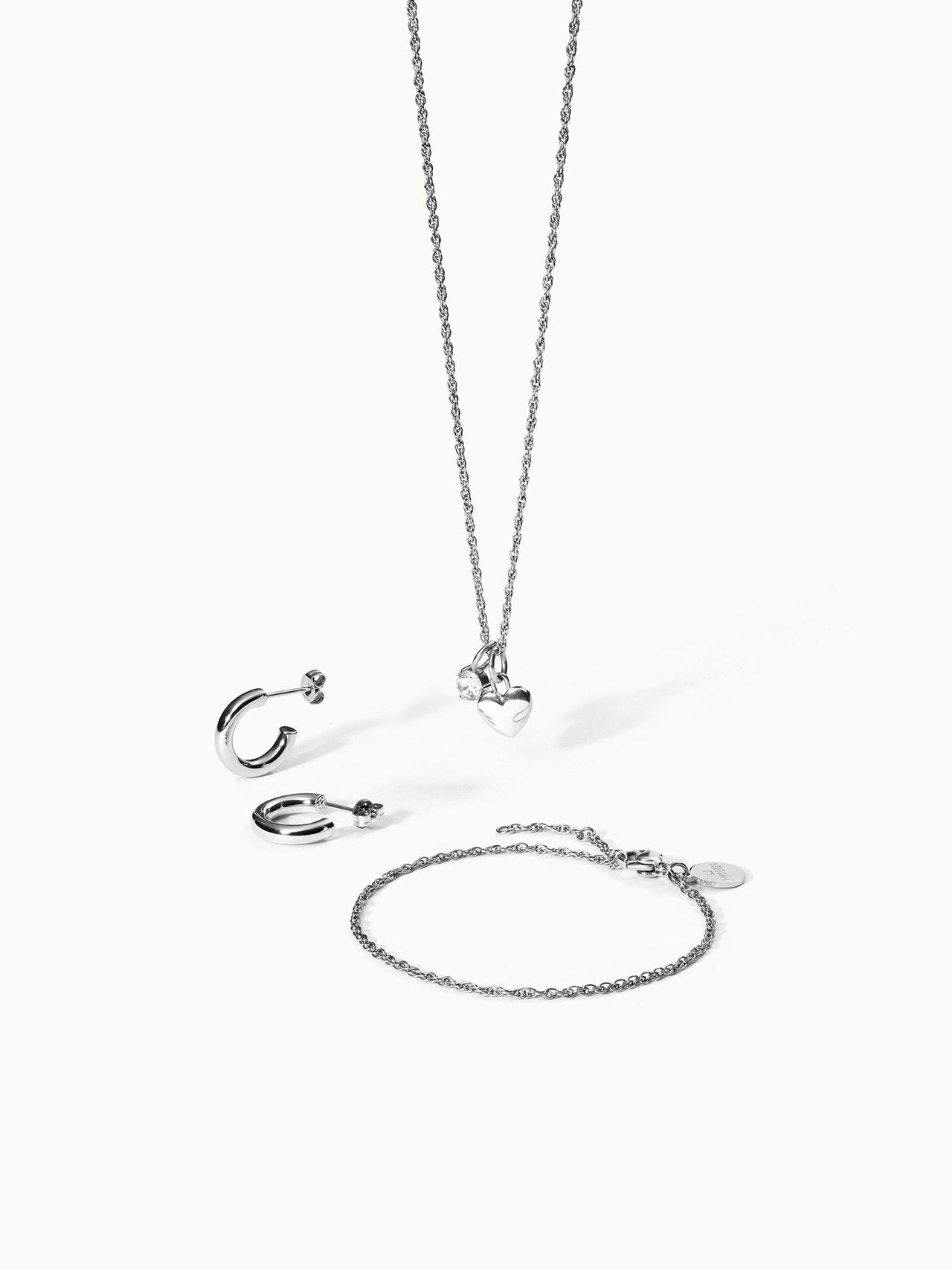 Silberne Schmuckstücke von PURELEI: Kette, Ohrringe und Armband mit Herzanhänger, elegant und modern.