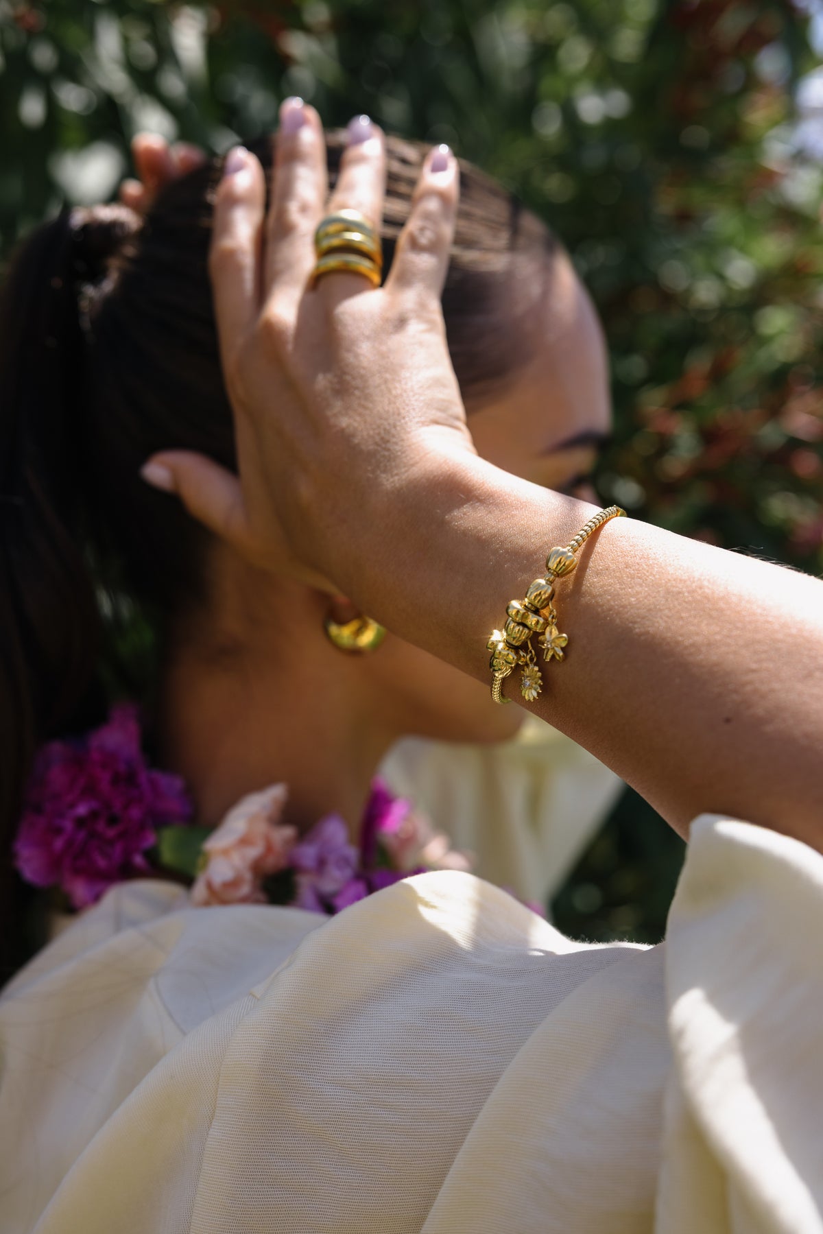 Roségoldenes Armband mit floralen Anhängern, getragen in sonniger, blühender Umgebung – PURELEI.