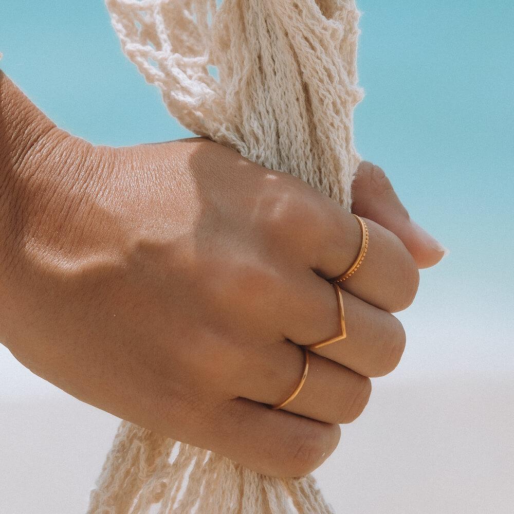 Filigraner Malihini Ring in 18K Gold mit V-Form, getragen an Hand vor hellem, sommerlichem Hintergrund von PURELEI.