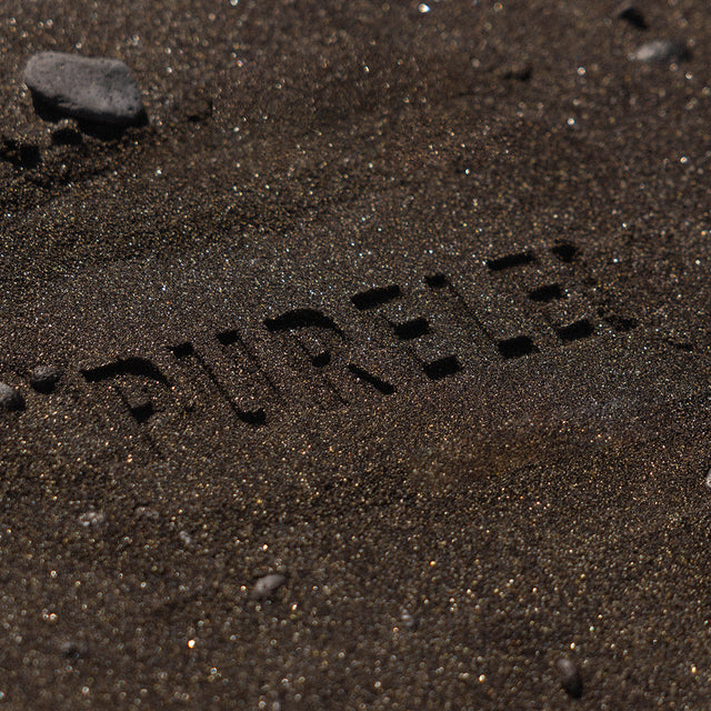 PURELEI in den Sand geschrieben, umgeben von feinem, dunklem Sand.