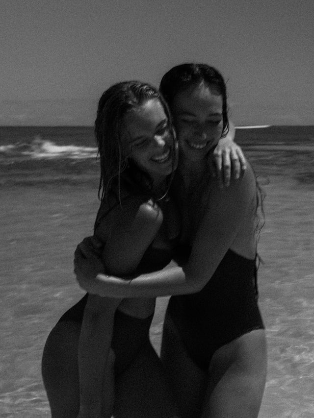 Zwei Frauen in schwarzen Badeanzügen am Strand, PURELEI inspiriert von Aloha-Vibes.
