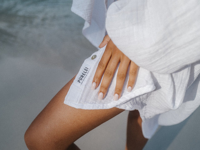 Helle, luftige PURELEI Bluse mit Logo, getragen am Strand, entspannte Sommerstimmung.