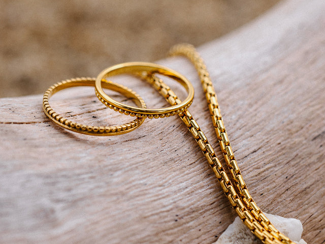 Drei goldene Ringe und eine Kette auf Holz, inspiriert von PURELEI.