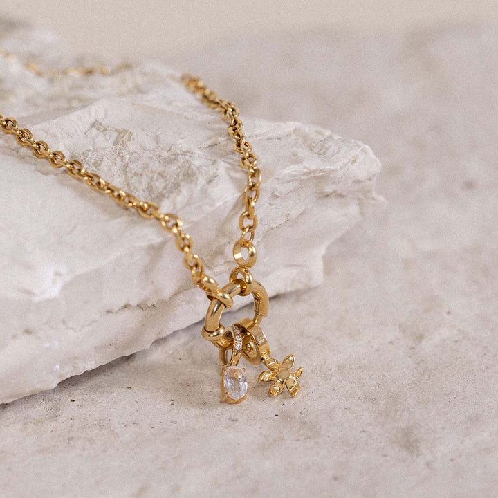 Goldene Kette mit funkelndem Anhänger auf hellem Stein, PURELEI inspiriert.