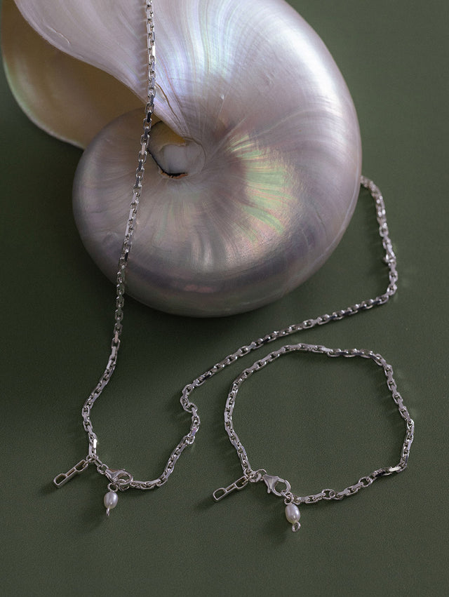 Silberne Kette und Armband mit Perlenanhänger, elegant auf Muschel präsentiert – PURELEI.