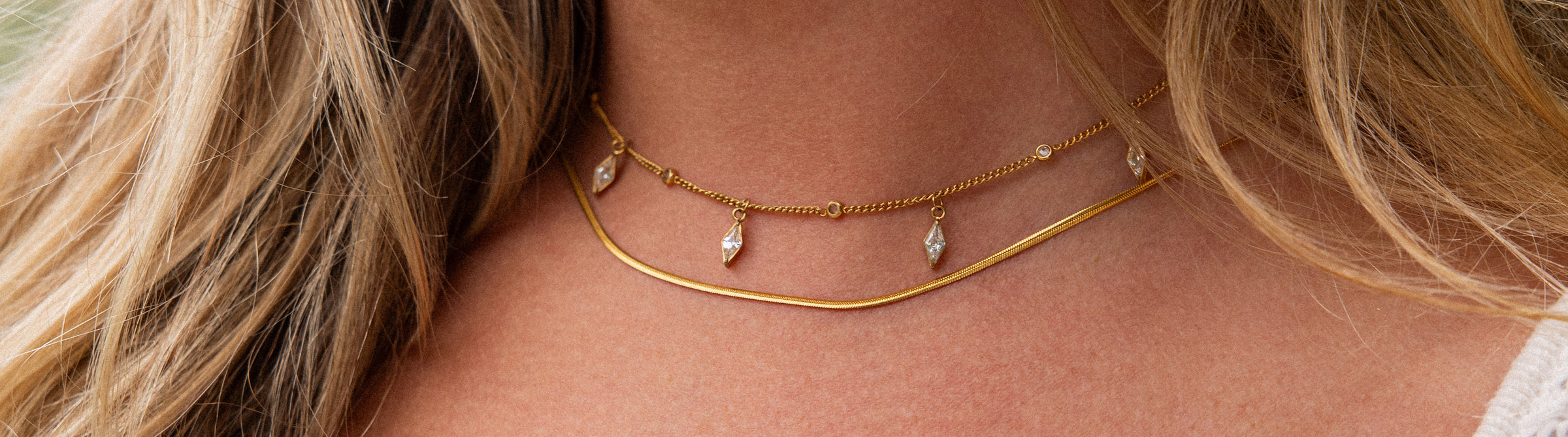 Zarte, roségoldene Kette mit Anhängern, getragen mit natürlichem Haar, PURELEI Stil.
