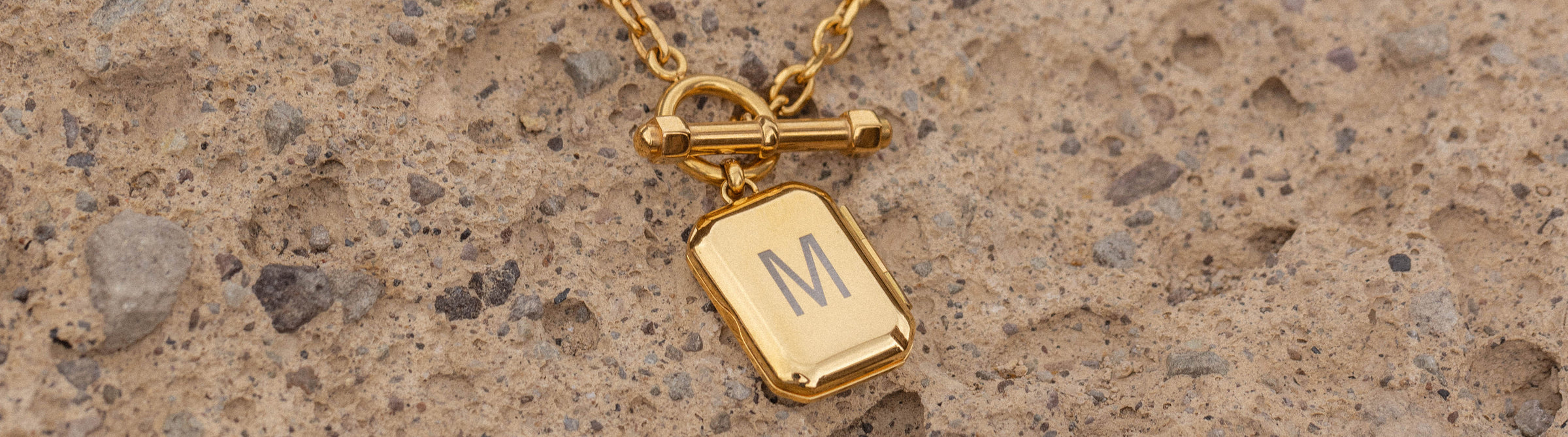 Goldene Kette mit graviertem M-Anhänger auf natürlichem Untergrund, PURELEI.