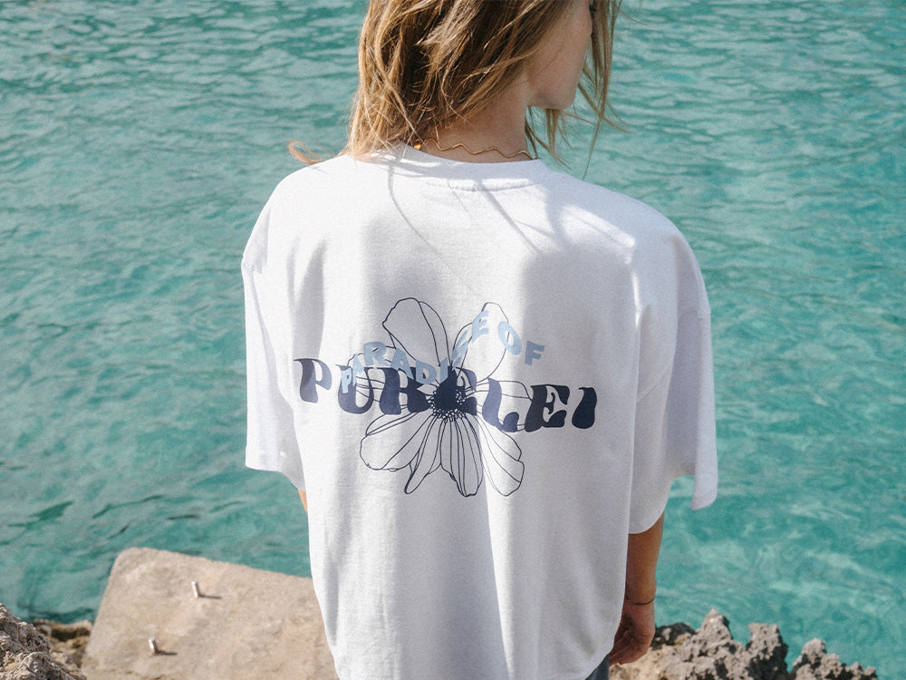 Weißes T-Shirt mit floralem PURELEI-Design, lässig am Wasser getragen.