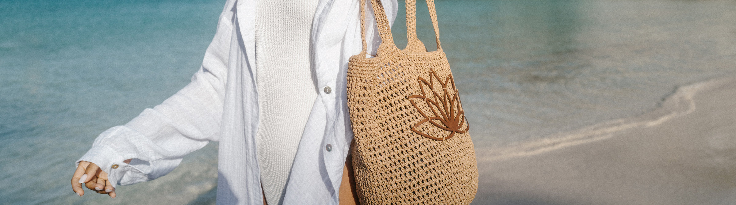 Helle, geflochtene Tasche mit Lotusmotiv, inspiriert von PURELEI, am Strand getragen.