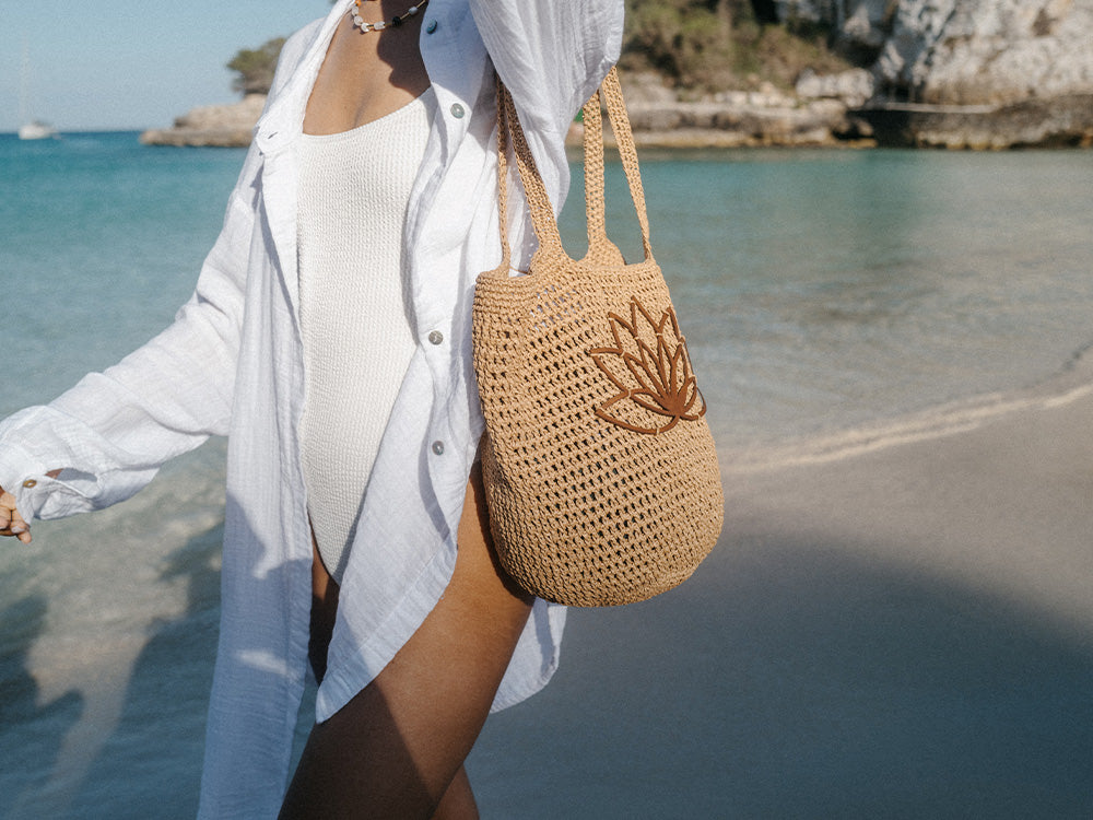 Braune, geflochtene Tasche mit Lotusmotiv am Strand, inspiriert von PURELEI.