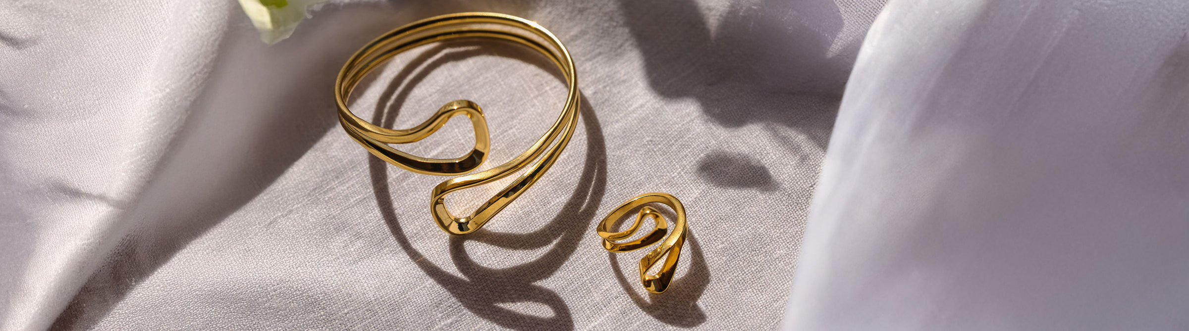 Goldenes, elegantes Armband und Ring auf sanftem Stoff, PURELEI inspiriert.