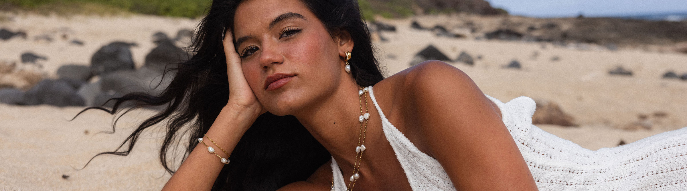 PURELEI Muschel-Schmuck in Gold und Perlen, getragen am Strand, strahlt tropische Eleganz aus.