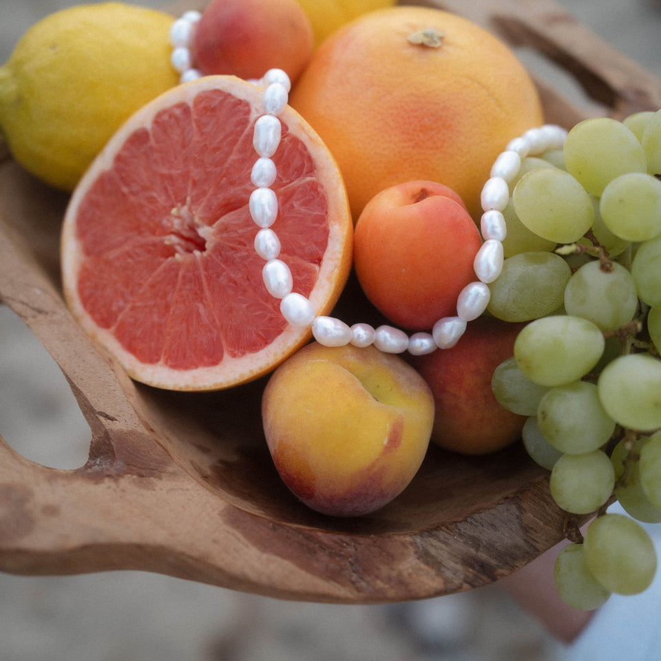PURELEI Moonlight Keshi Kette mit großen weißen Perlen auf Holzschale mit Sommerfrüchten, elegant und natürlich.