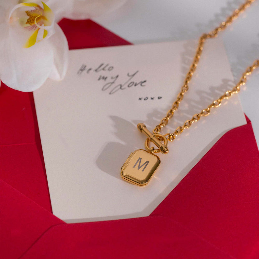 Roségoldene Kette mit M-Anhänger, elegant auf rotem Briefumschlag inszeniert – PURELEI.