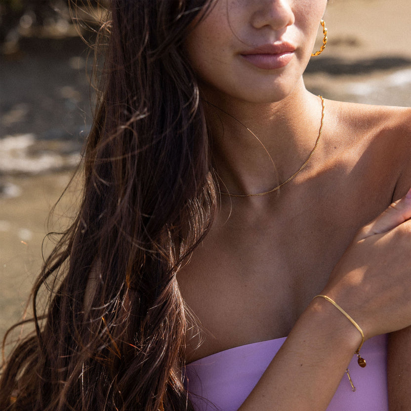 Feine PURELEI Kaula Kette in 18K Gold mit gedrehtem Design, getragen in natürlichem, sonnigem Strandambiente.