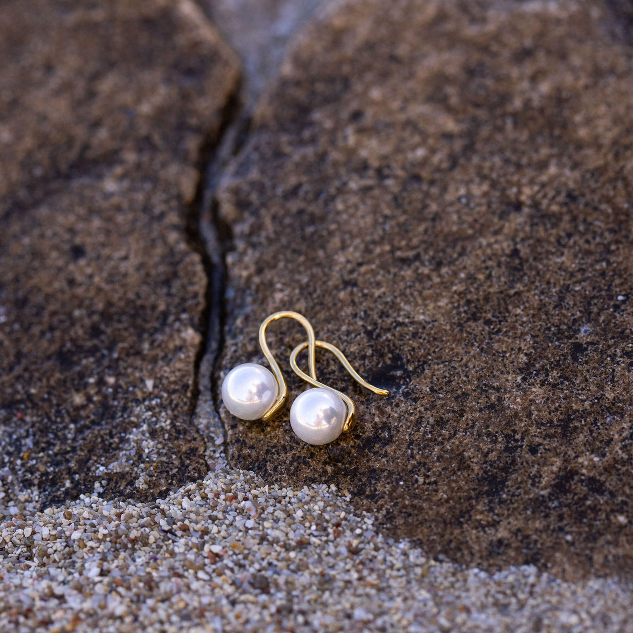 PURELEI Pure Pearl Ohrringe mit goldenen Muschel-Perlen, elegant auf rauem Stein, Insel-Spirit und zeitlose Schönheit.