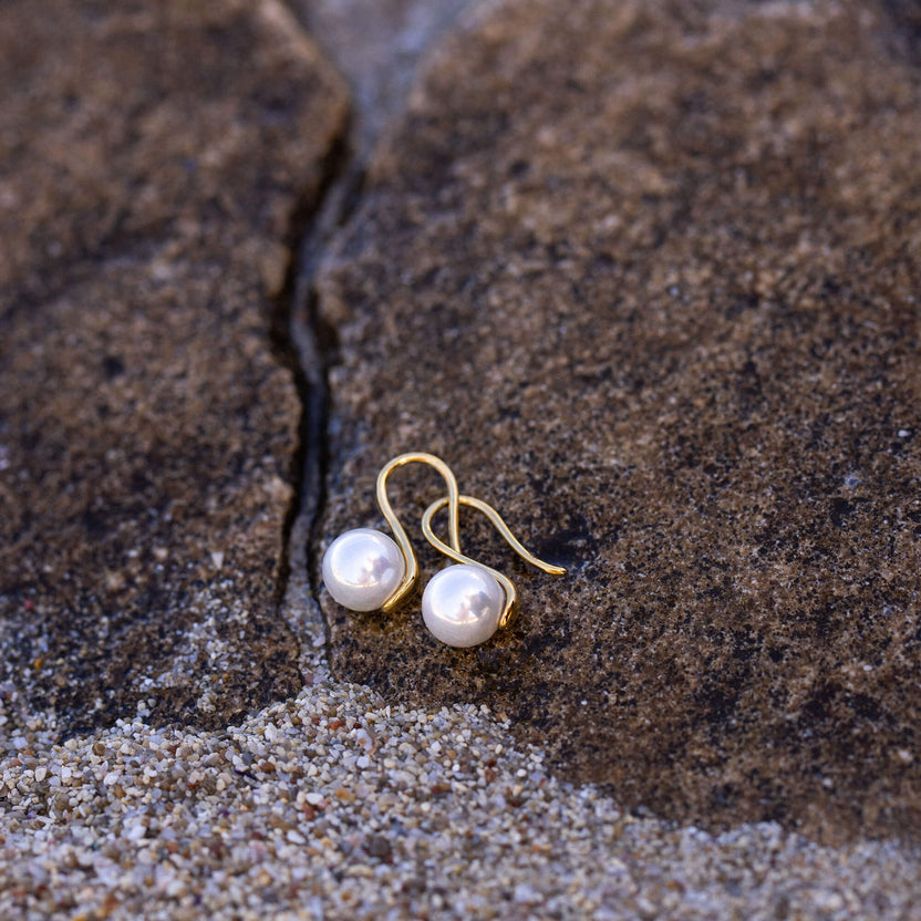 PURELEI Pure Pearl Ohrringe mit goldenen Muschel-Perlen, elegant auf rauem Stein, Insel-Spirit und zeitlose Schönheit.