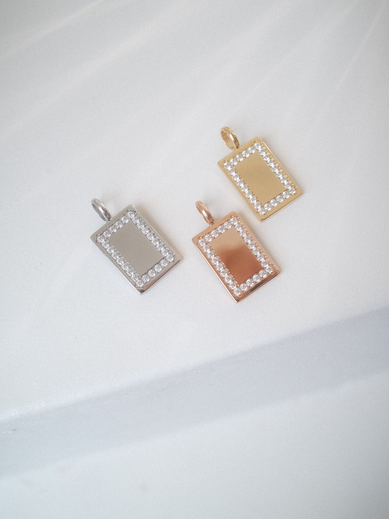 Glimmer Charm in Gold, Silber und Roségold mit Zirkonia-Rahmen, elegant auf hellem Hintergrund, PURELEI.
