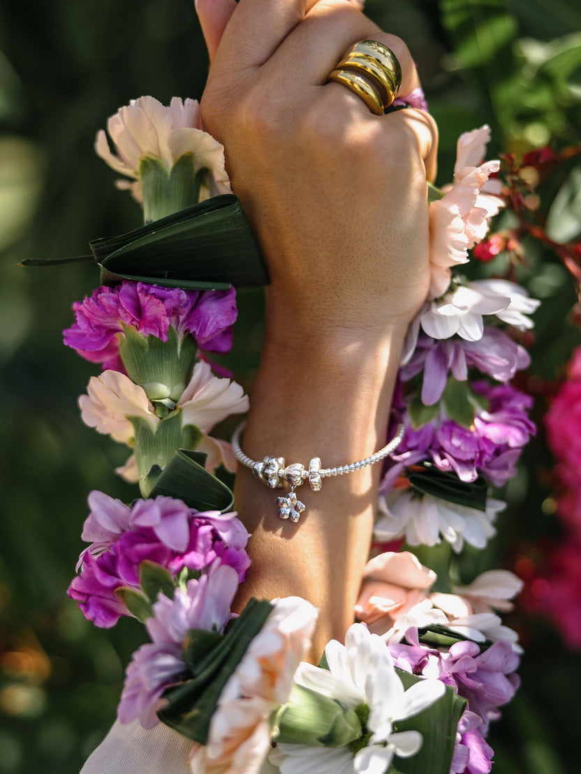 PURELEI Lei Herz Bubble Charm in Silber, herzförmig, zart am Handgelenk mit tropischem Blumenschmuck getragen.