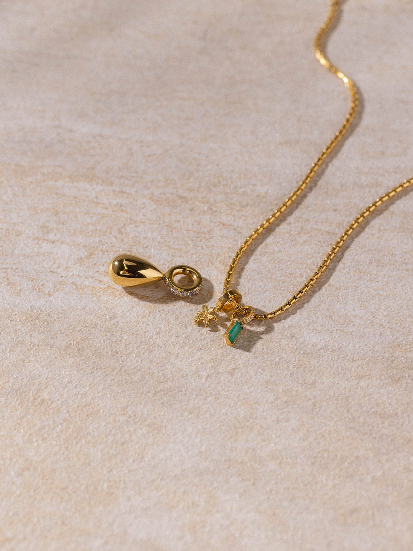 PURELEI Resonance Kette aus 18K vergoldetem Edelstahl mit zartem Anhänger auf sandigem Untergrund, elegant und zeitlos