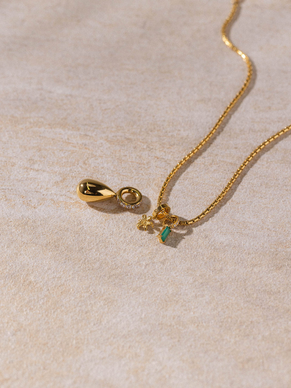 PURELEI Resonance Kette aus 18K vergoldetem Edelstahl mit zartem Anhänger auf sandigem Untergrund, elegant und zeitlos
