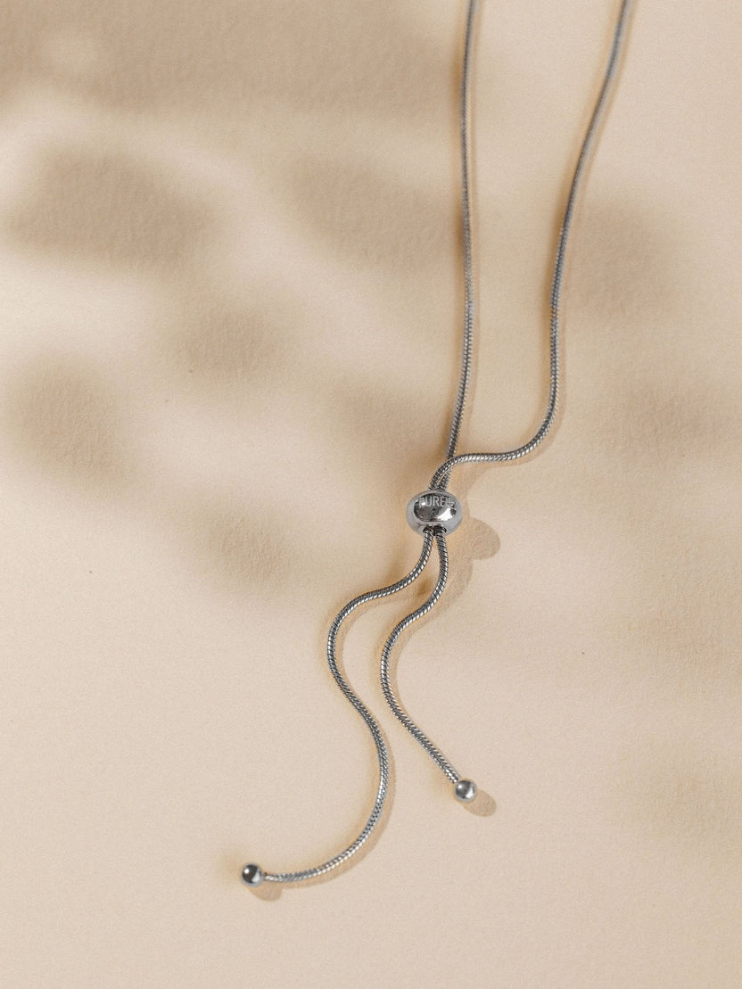 Silberne Kette mit geschwungenem Design, PURELEI, elegant auf beigem Hintergrund.