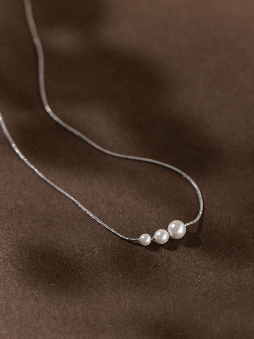 Zarte PURELEI Kette mit drei matten, runden Anhängern auf dunklem Hintergrund.