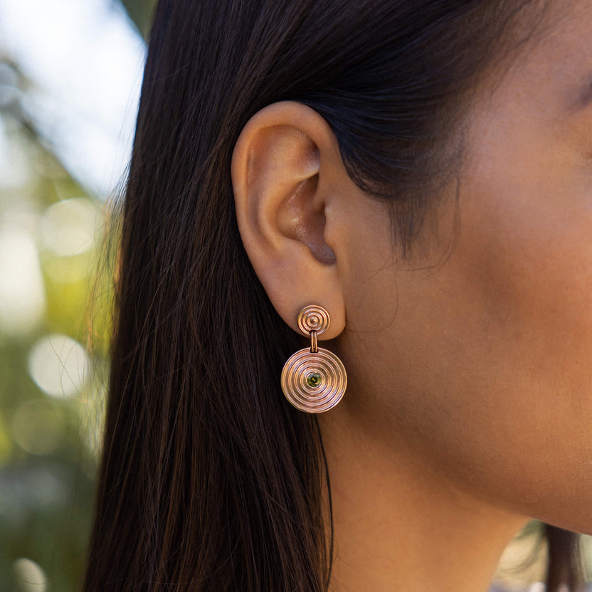 Artistic Ohrringe aus roségoldenem Edelstahl mit zwei Ringen und grün funkelndem Zierstein, elegant am Ohr.