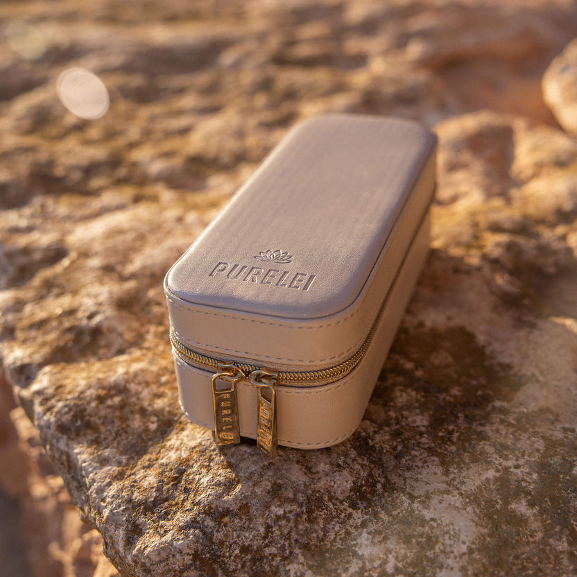 Beige Schmuckbox von PURELEI mit goldenen Reißverschlüssen auf steiniger Oberfläche.