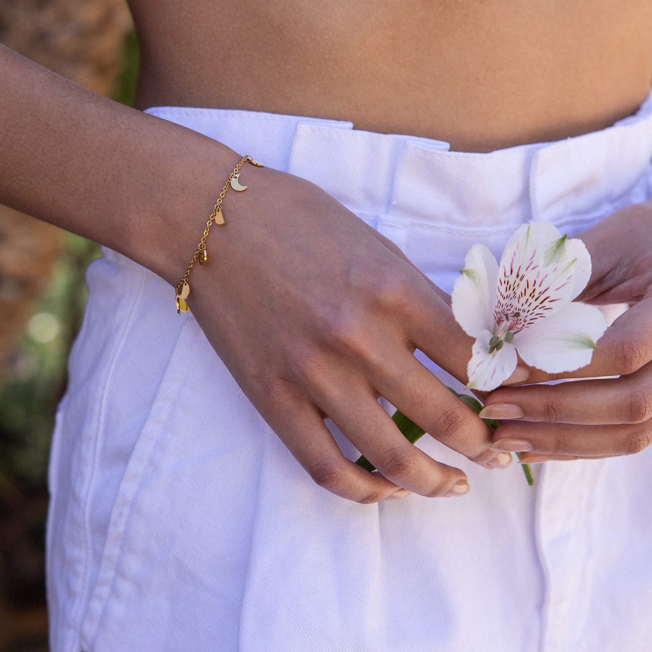 Goldenes Armband mit Mond- und Herzanhängern, getragen mit einer Blume, PURELEI.