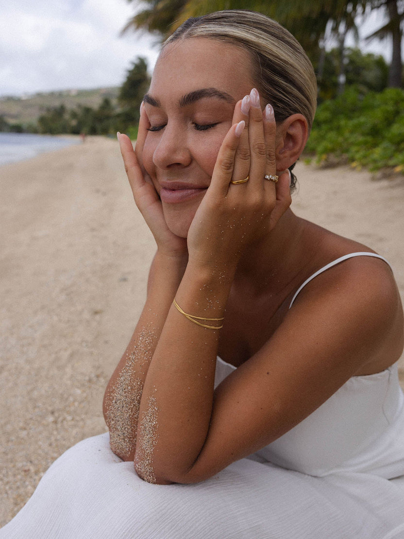 Feminines PURELEI Armband aus Roségold, getragen am Strand, umgeben von sandiger Atmosphäre.