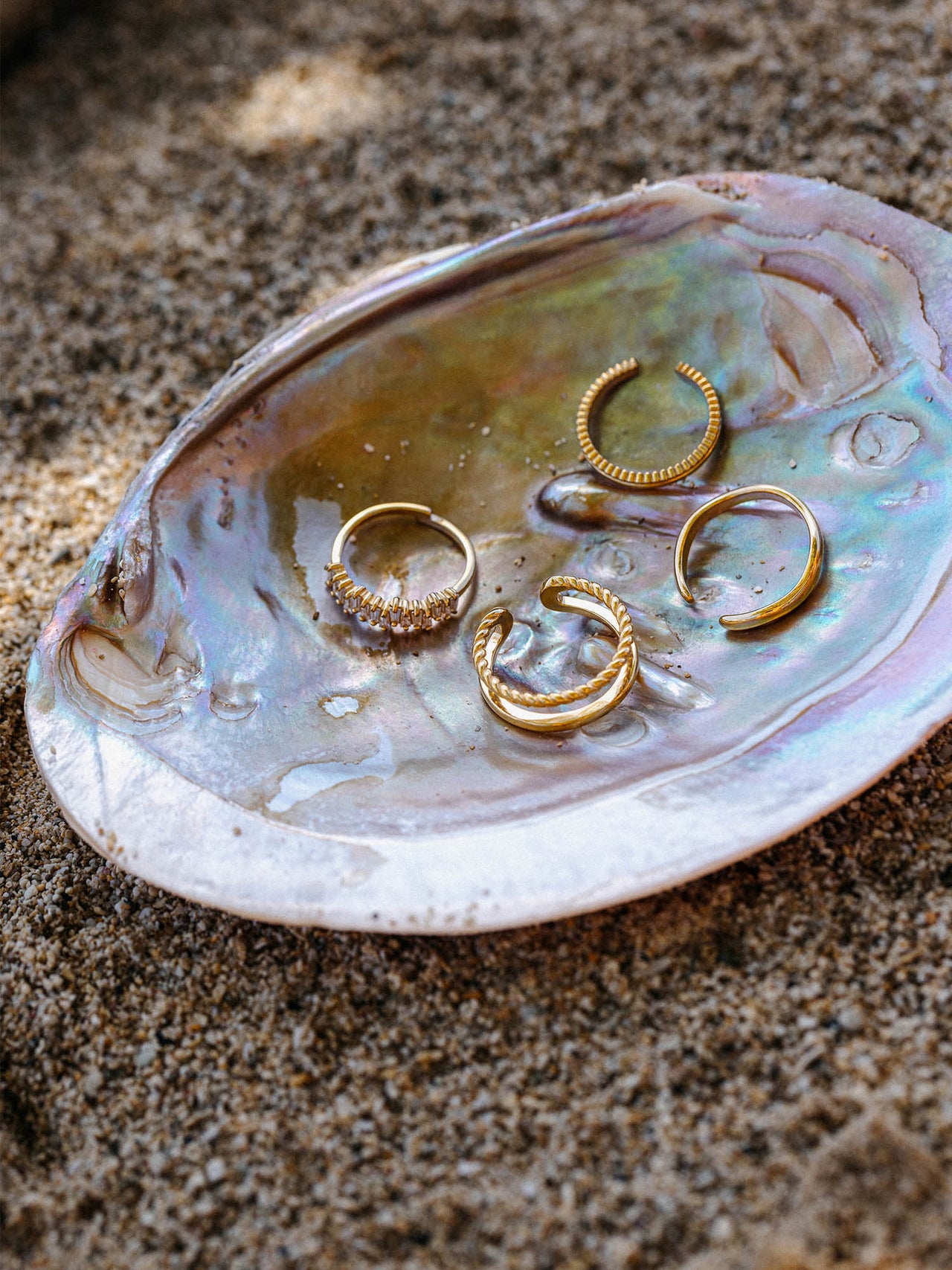 Silberne Ringe auf einer Muschel, inspiriert von PURELEI, am Sand platziert.