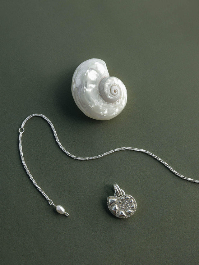 Silberne Kette mit Muschel-Anhänger auf grünem Hintergrund, inspiriert von PURELEI.