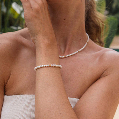 Weiße Perlenkette und Armband von PURELEI, elegant und feminin, umgeben von tropischer Atmosphäre.