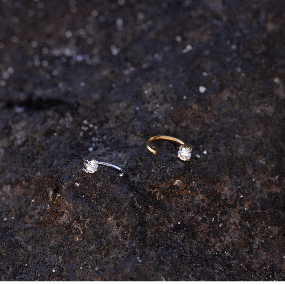 Highlight Piercing von PURELEI, gold- und silberfarbene Edelstahlringe mit funkelndem Zirkonia auf dunklem Lavagestein.