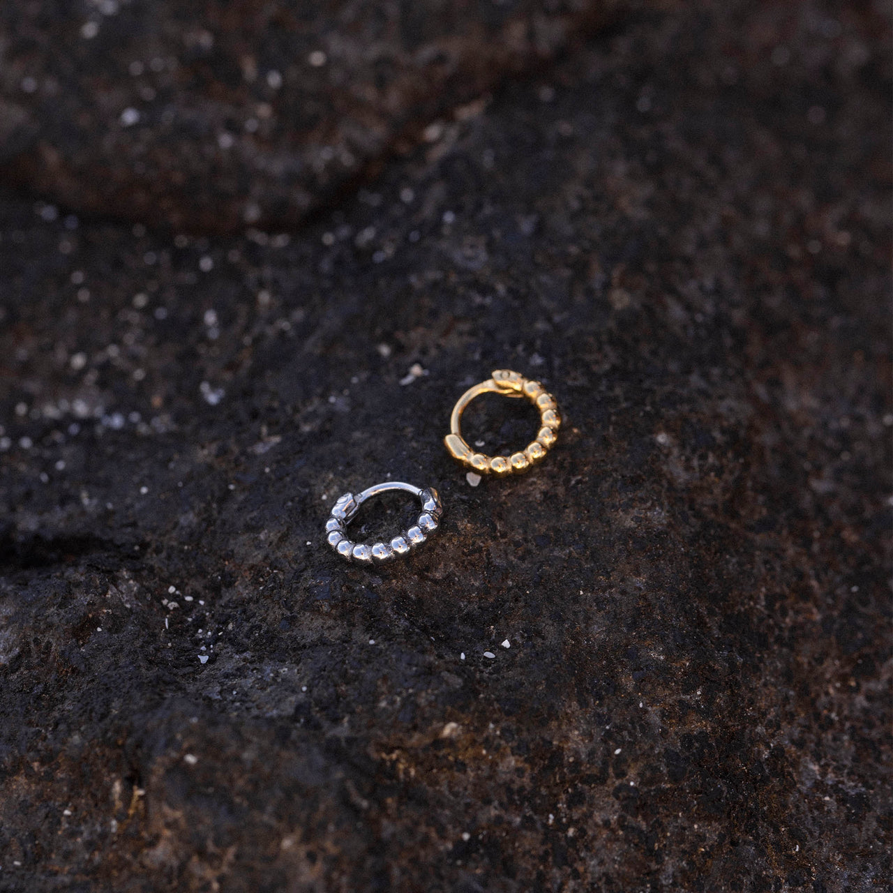 PURELEI Spherical Piercing in Gold und Silber mit kugeligem Design auf dunklem Lavagestein, elegant und nickelfrei