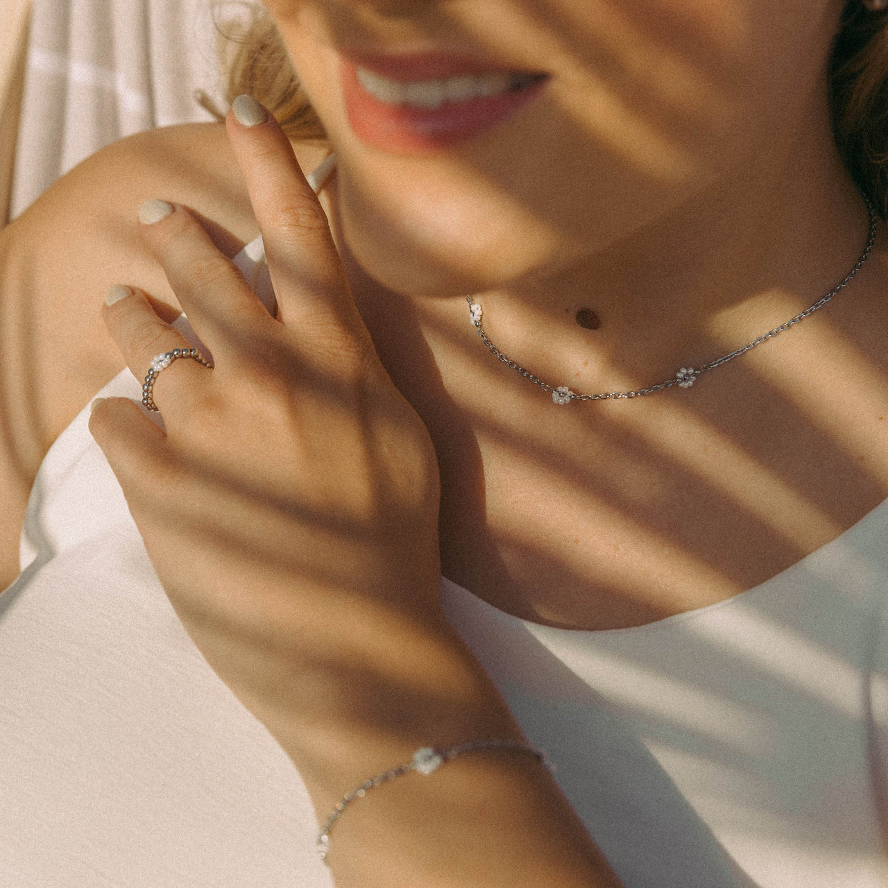 Silberne Kette und Ring mit Blumenmotiven, PURELEI, in warmem Licht, elegant und feminin.