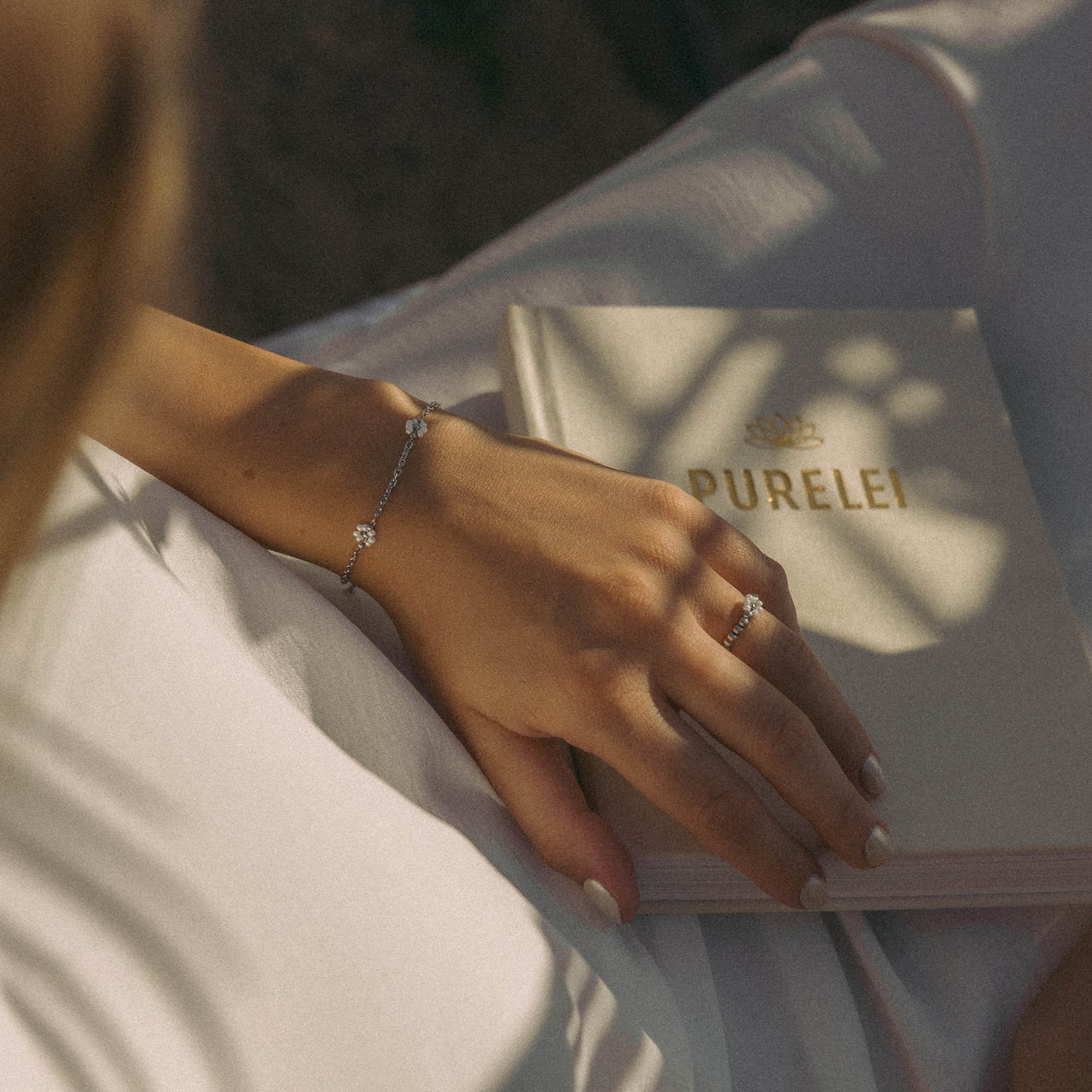 Silbernes Armband mit funkelnden Details, getragen mit PURELEI Buch im Hintergrund.