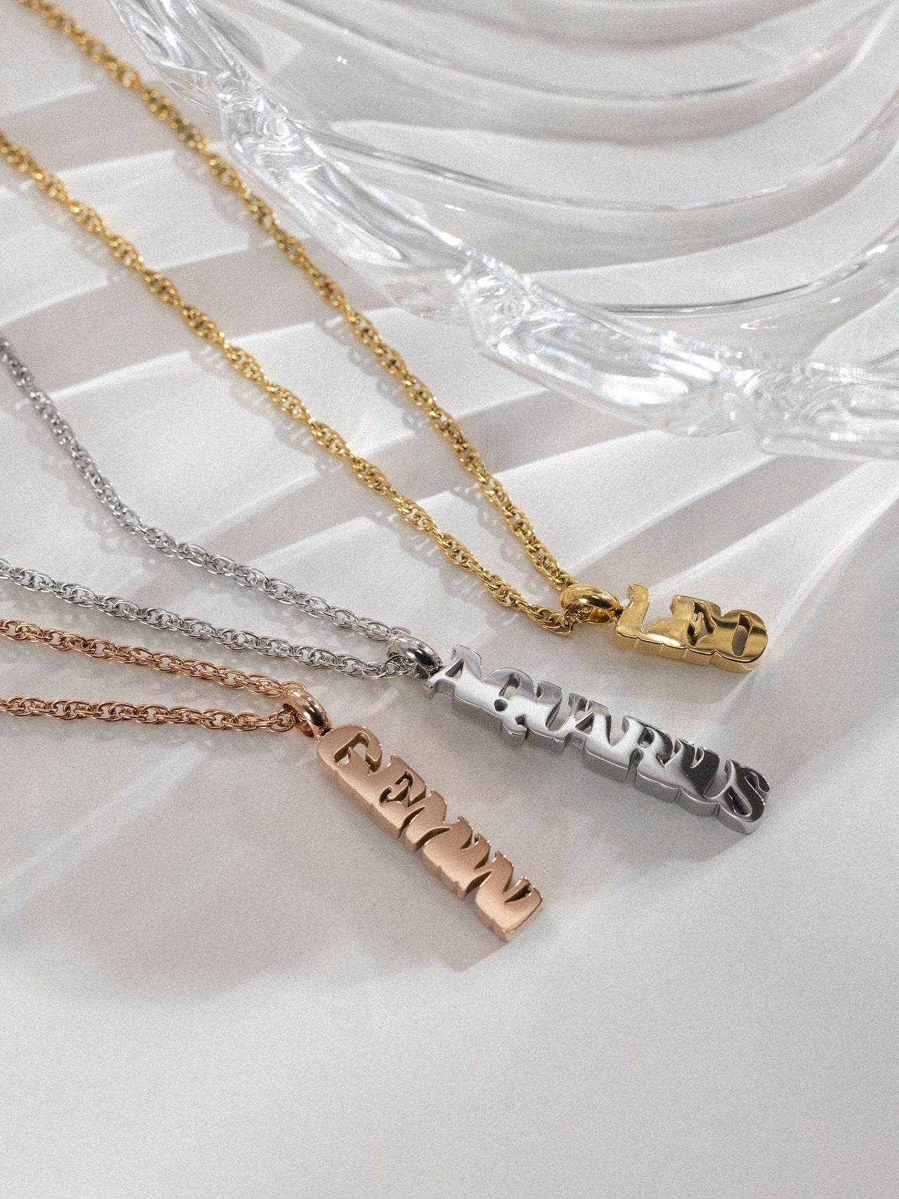 Gemini Letter Charm in Gold, Silber und Roségold auf heller Oberfläche, edel und feminin, PURELEI.