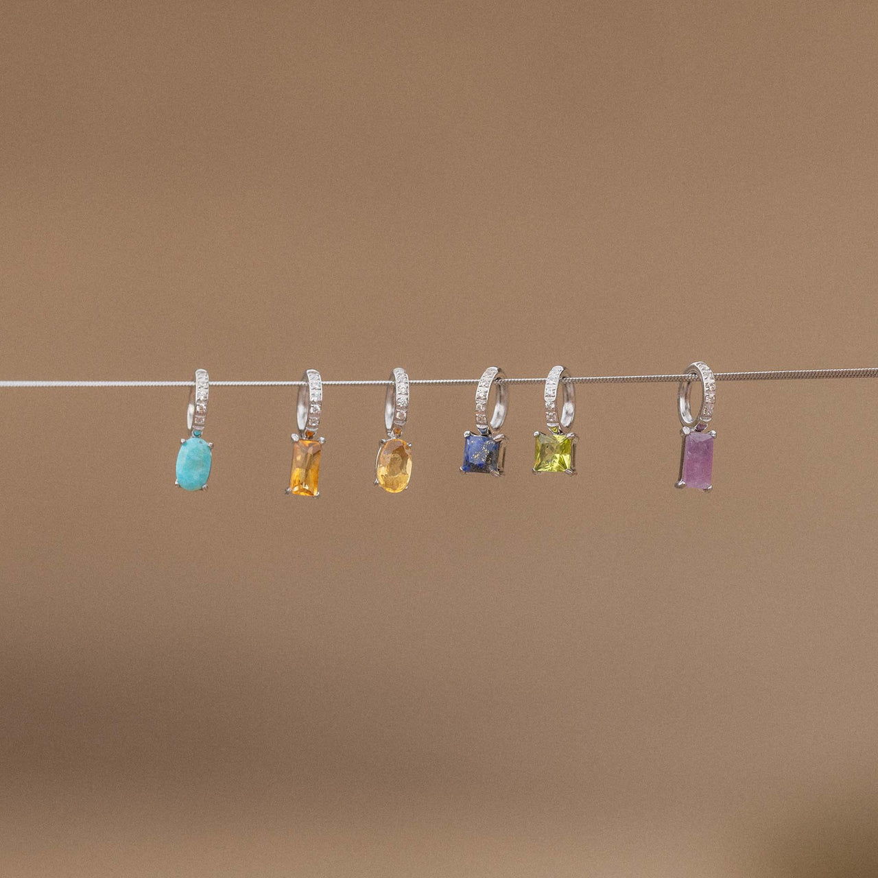 Sechs elegante PURELEI Anhänger mit bunten Steinen und funkelnden Details auf einem Draht.