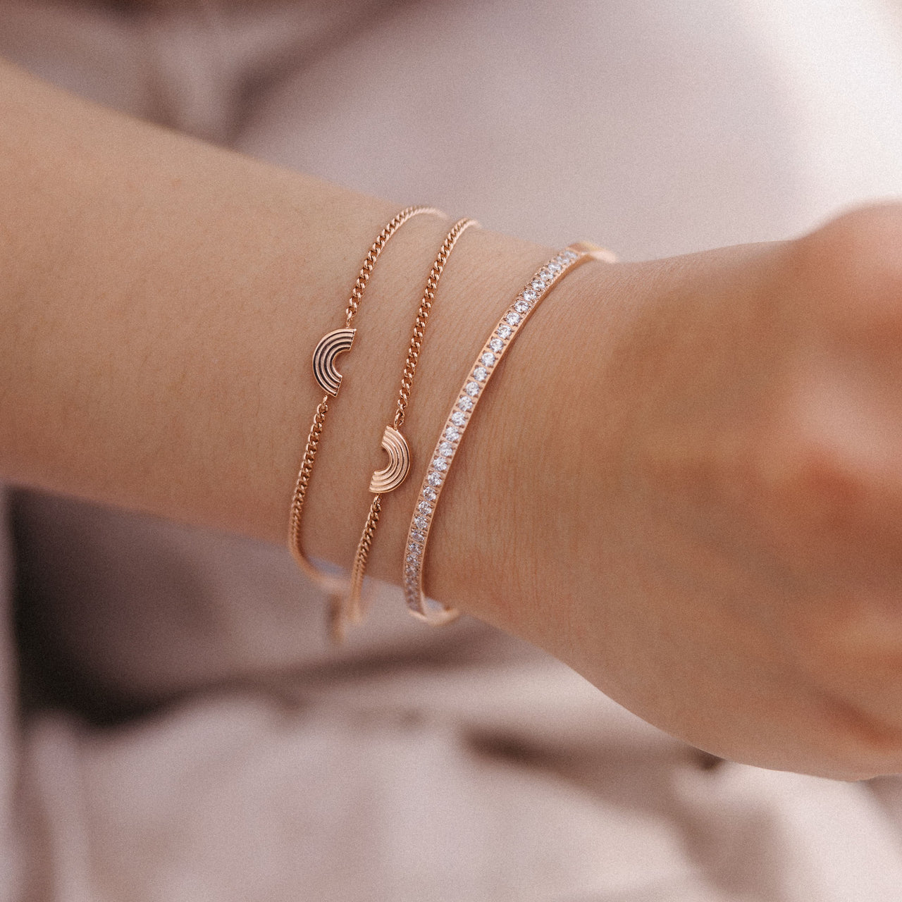 Drei roségoldene Armbänder mit Wellen- und Glitzerdesign von PURELEI am Handgelenk.