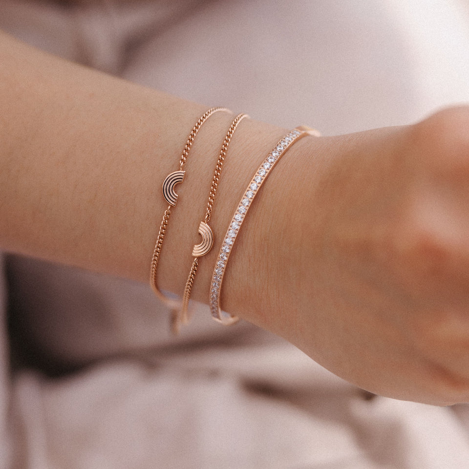Drei roségoldene Armbänder mit Wellen- und Glitzerdesign von PURELEI am Handgelenk.