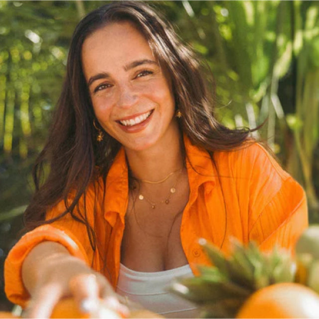 Frau mit orangefarbenem Shirt und PURELEI Schmuck, umgeben von tropischer Natur.