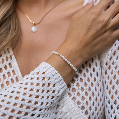 Weißes Armband aus Muscheln, getragen mit zartem Anhänger von PURELEI.