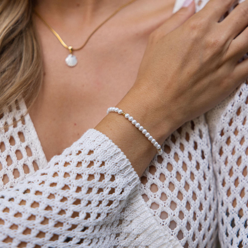 Weißes Armband aus Muscheln, getragen mit zartem Anhänger von PURELEI.