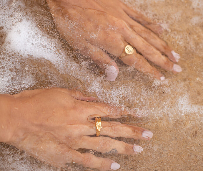 Goldene Ringe von PURELEI in Wasser, elegant und feminin, umgeben von sanften Wellen.