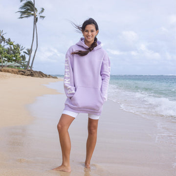 Helle PURELEI Kapuzenjacke am Strand, umgeben von tropischer Atmosphäre.