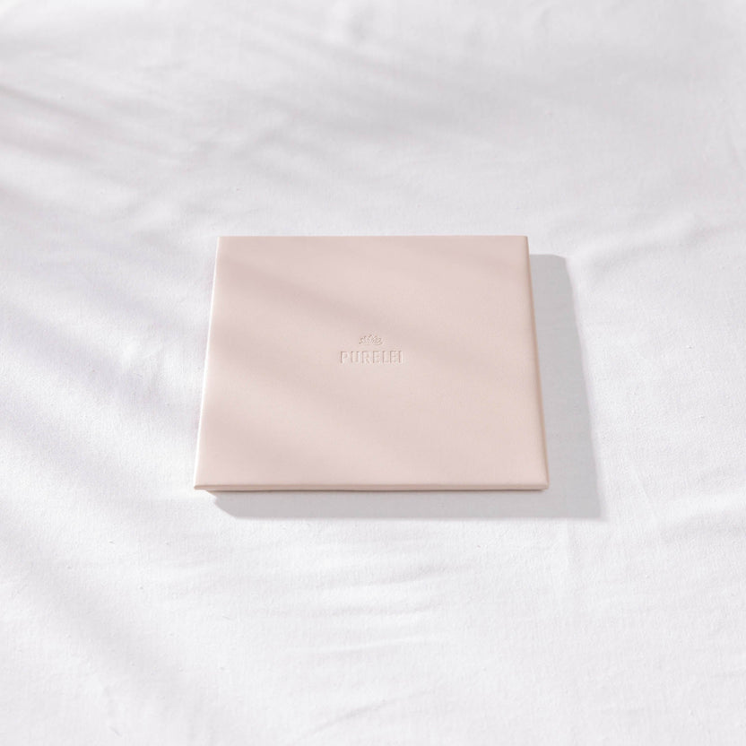 Zarte, rosa PURELEI Schmuckbox auf weißem Stoff, elegant und minimalistisch.